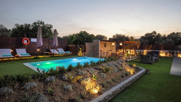 A pool with lounge chairs, a covered seating area, and a stone wall. - Kathys Apartment 2 in Archaggelos (Αρχαγγελος)