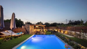 A swimming pool with lounge chairs and a table, surrounded by a wooden fence and greenery. - Kathys Apartment 2 in Archaggelos (Αρχαγγελος)