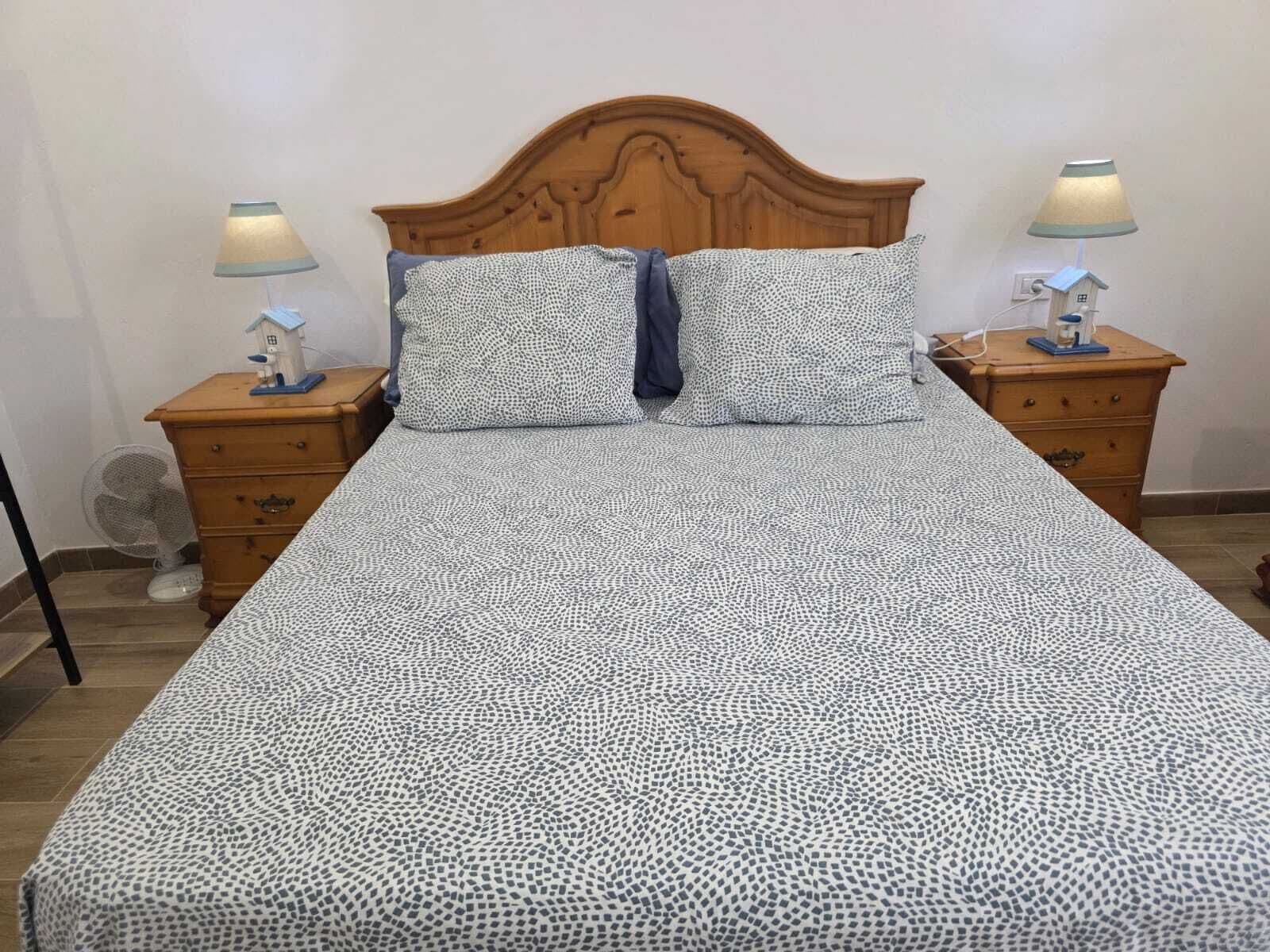 A bed with a patterned bedspread, two nightstands with lamps, and a wooden headboard.
