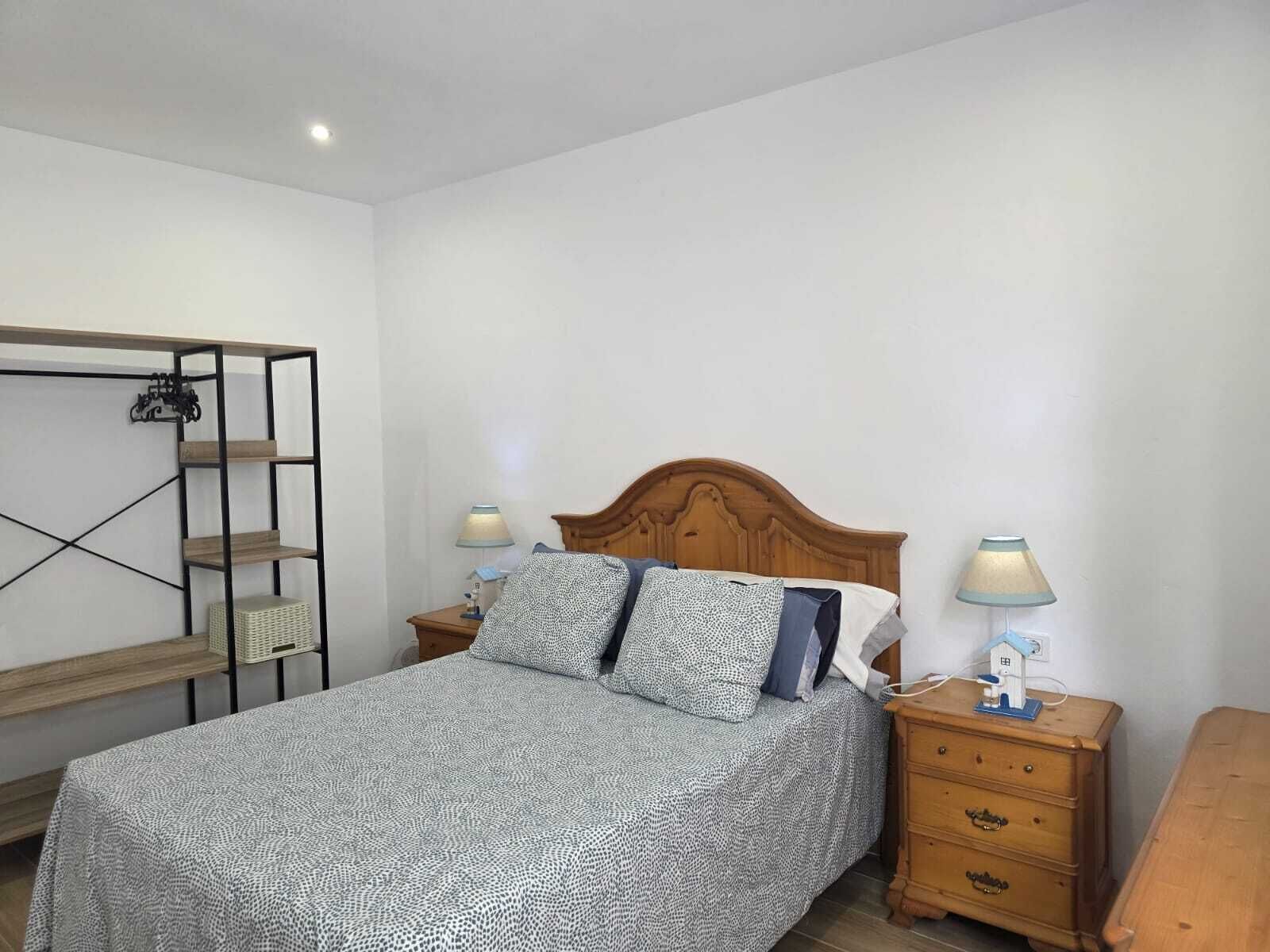 A bedroom with a bed, two bedside tables, a nightstand, a wooden bench, and a wall-mounted shelf.