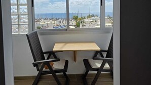 Habitación con una ventana grande que ofrece vistas al mar y al paisaje urbano. Hay una pequeña mesa y dos sillas.