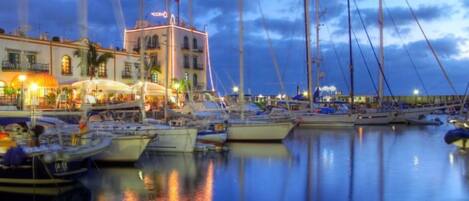 Ein Yachthafen mit mehreren Schiffen, ein Gebäude mit einem Turm und ein Restaurant am Wasser.