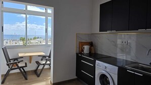 Una cocina compacta con lavadora, un comedor con vista al mar y un ventanal grande.