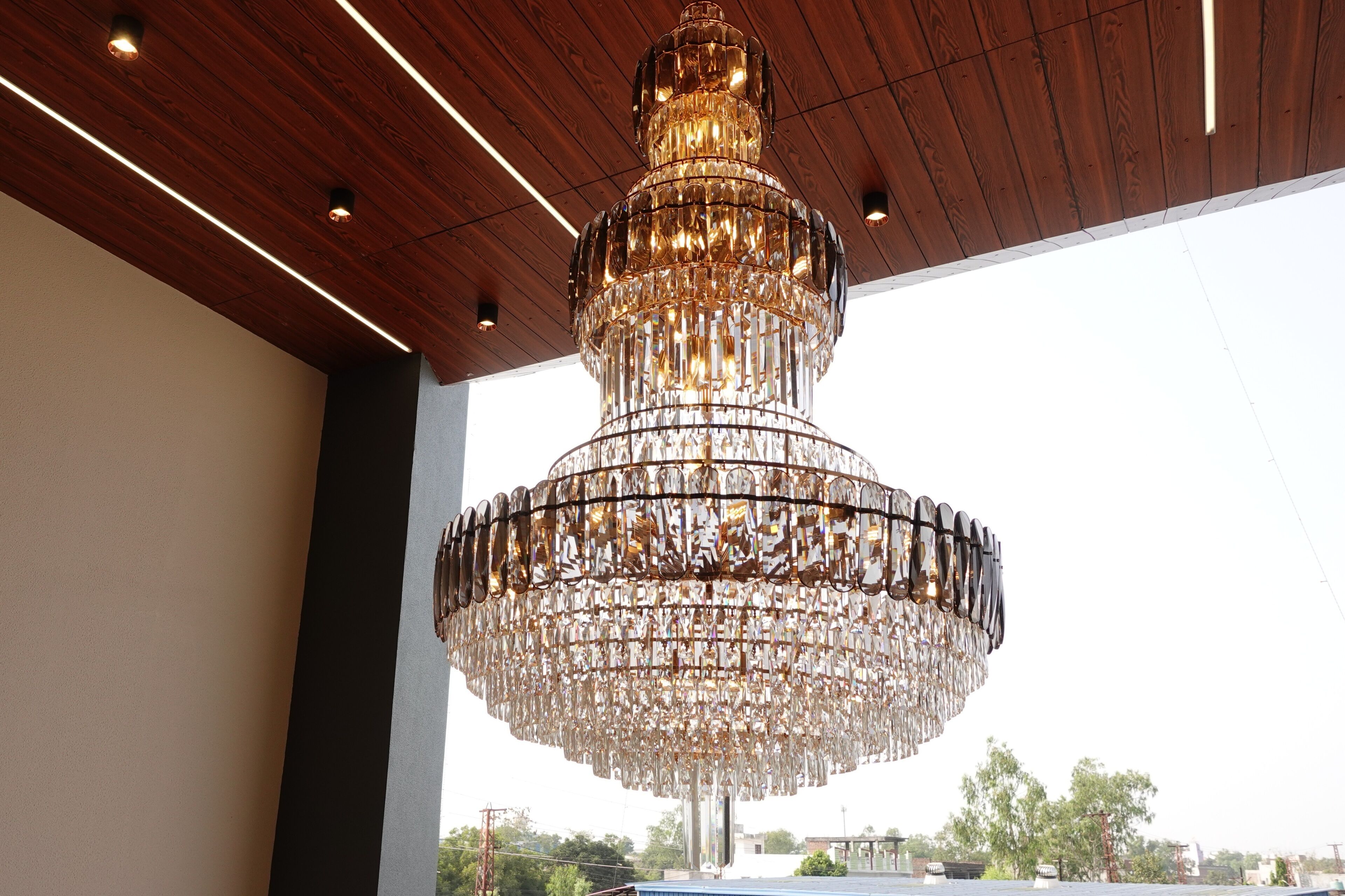 A large, ornate chandelier hanging from a wooden ceiling in a spacious room with a view of the cityscape.