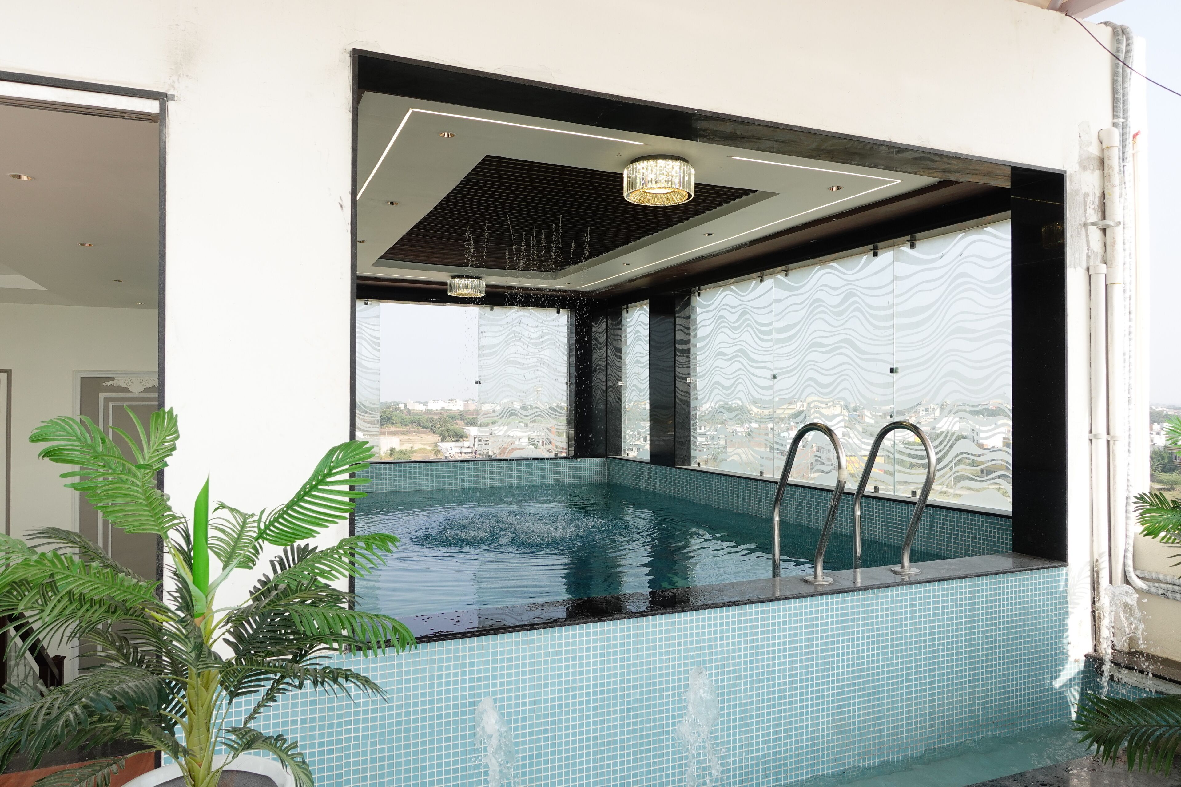 Una piscina interior moderna con vistas a la ciudad, rodeada de amplios ventanales y un techo con una lámpara de diseño único.