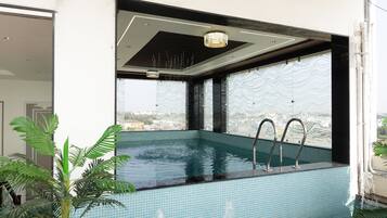 Una piscina interior moderna con vistas a la ciudad, rodeada de amplios ventanales y un techo con una lámpara de diseño único.