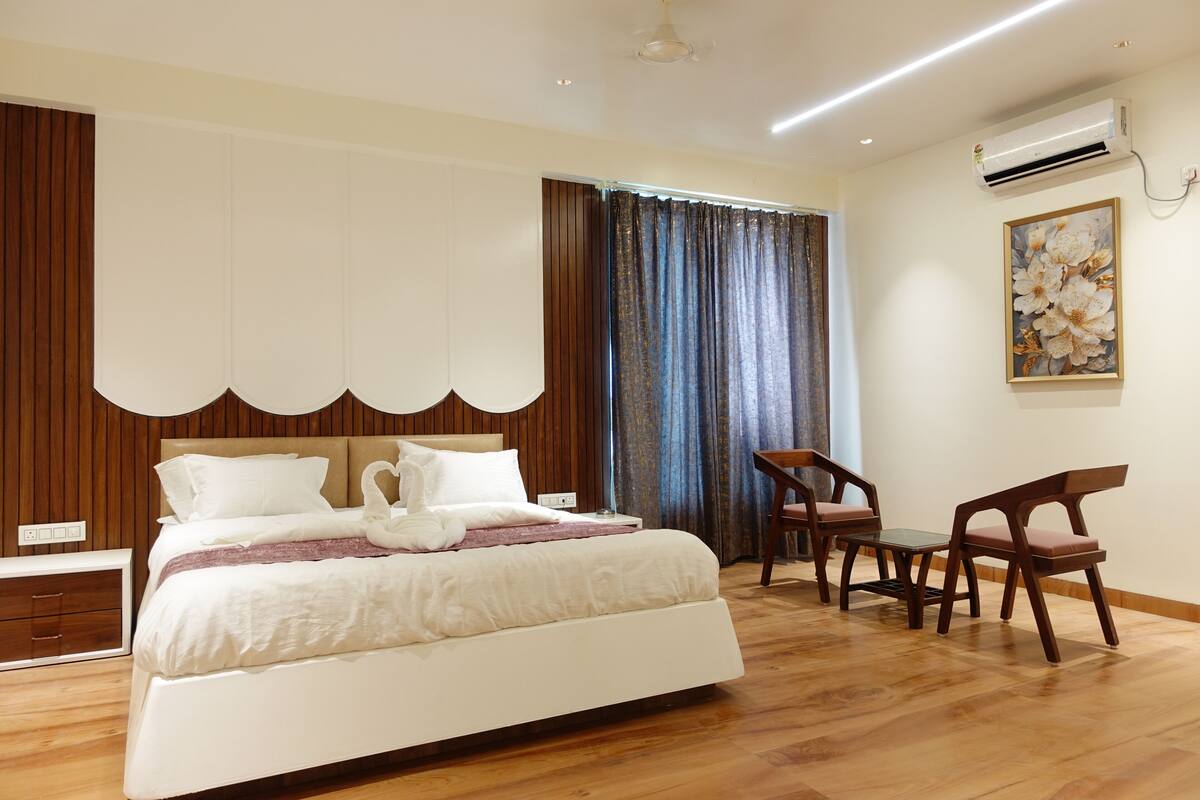 Une chambre d’hôtel moderne dotée d’un grand lit, de lambris en bois, d’un bureau avec des chaises et d’un appareil de climatisation.