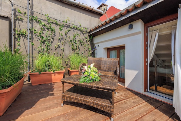 A wicker chair on a wooden deck with potted plants, a sliding glass door, and a wall with climbing plants.