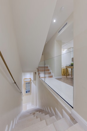 A staircase with white steps and a glass railing, leading to a landing with a table and a yellow tablecloth. - Cà dell'Arte Boutique (Venice)
