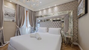 A neatly made bed with white linens, a tufted headboard, and a bedside table with a mirror and a lamp. - Cà dell'Arte Boutique (Venice)
