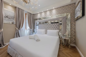 A neatly made bed with white linens, a tufted headboard, and a bedside table with a mirror and a lamp.