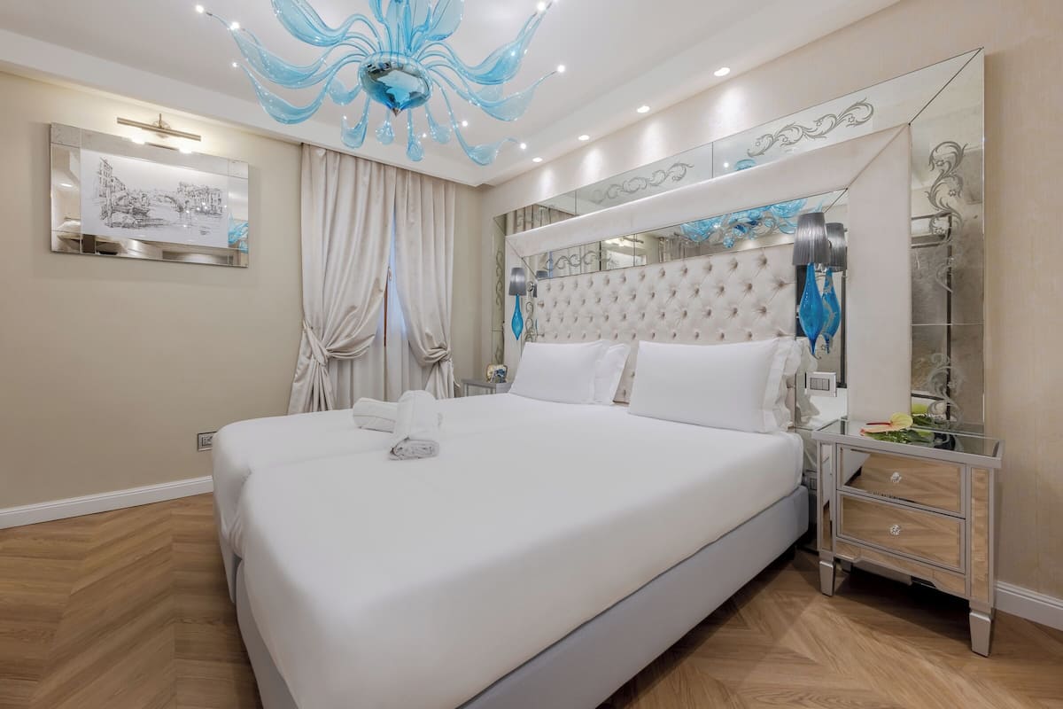 A spacious bedroom with a large bed, a mirror, a chandelier, and a wooden floor.