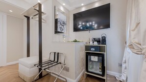 A hotel room with a flat-screen TV, a minibar, a small refrigerator, a seating area with a chair, and a wall-mounted mirror. - Cà dell'Arte Boutique (Venice)