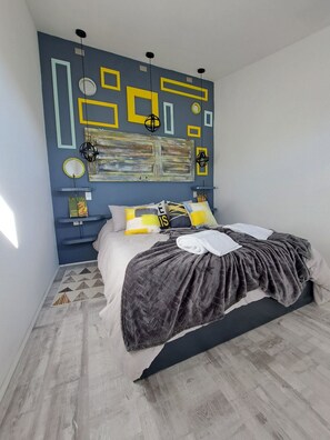 A bedroom with a bed, a wall art piece, and a wooden floor.