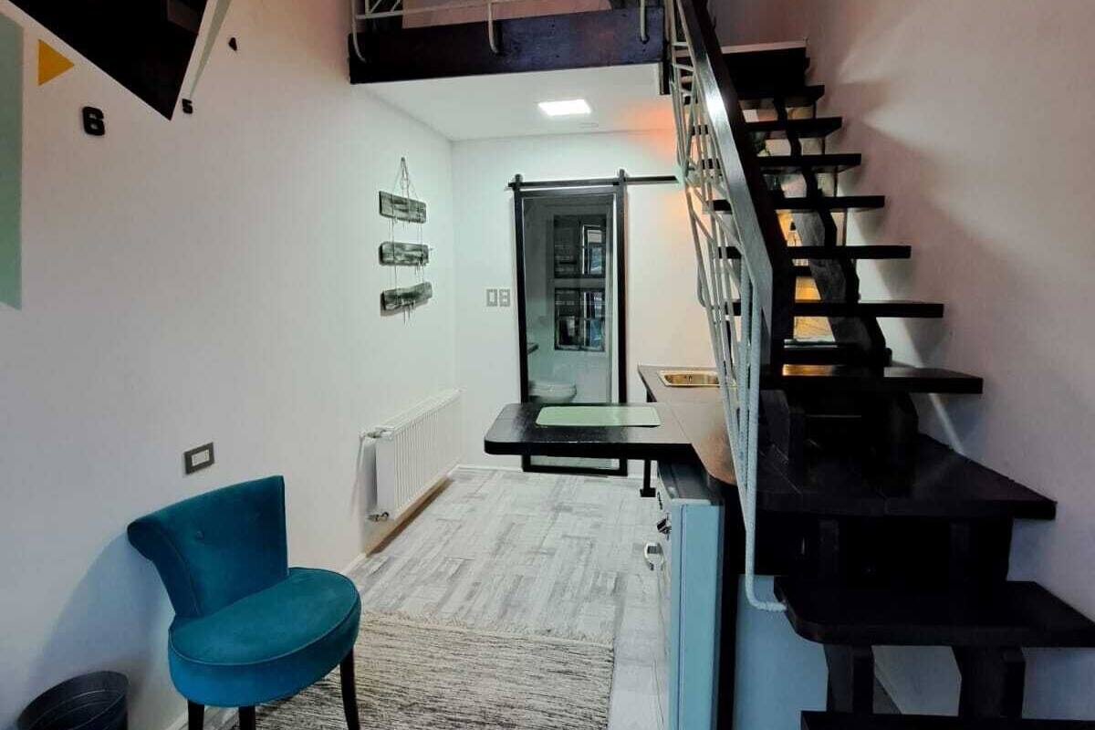 Un interior moderno con una escalera, sillas color turquesa y una zona de cocina.