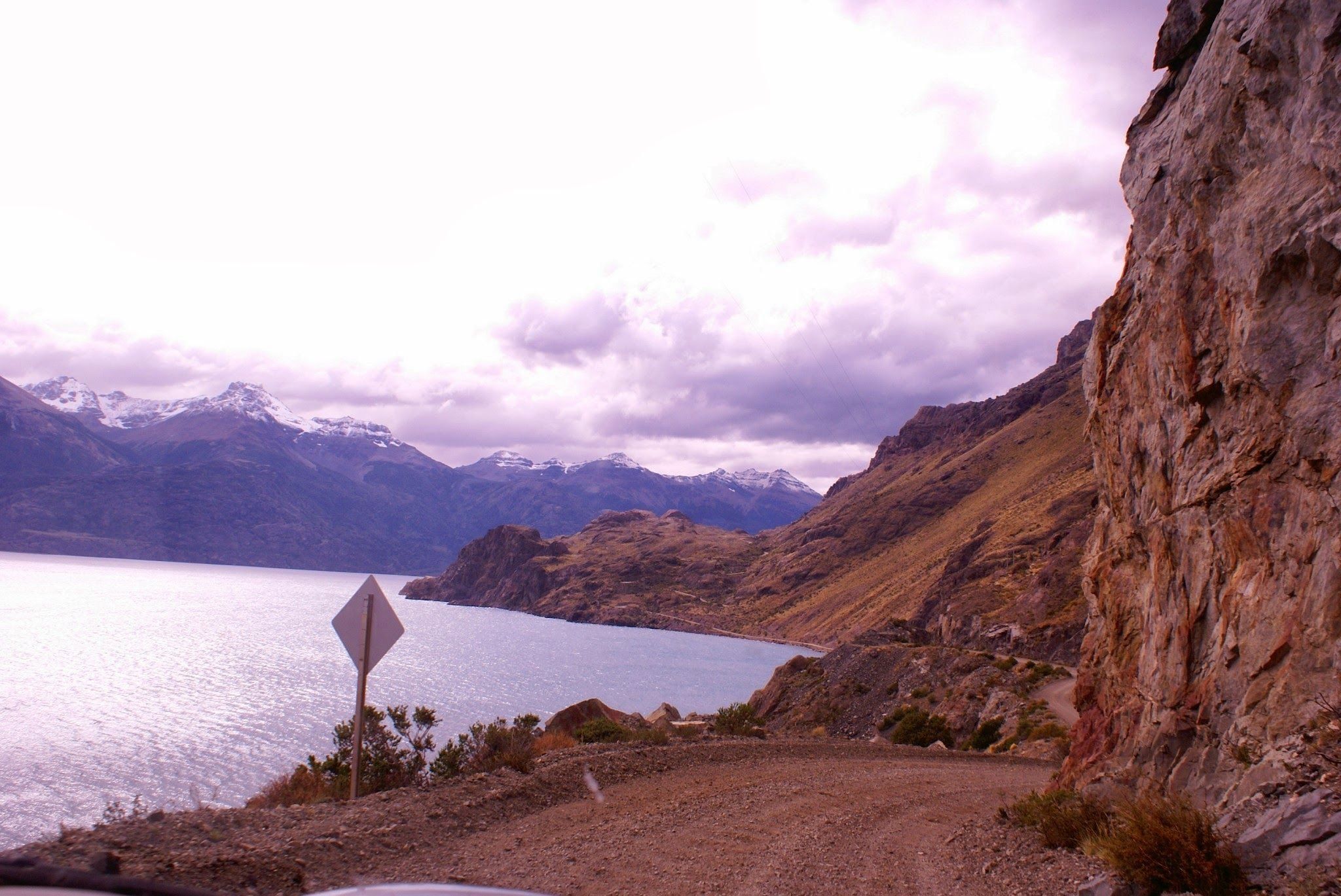 A mountainous landscape with a lake, a road, and a signpost.