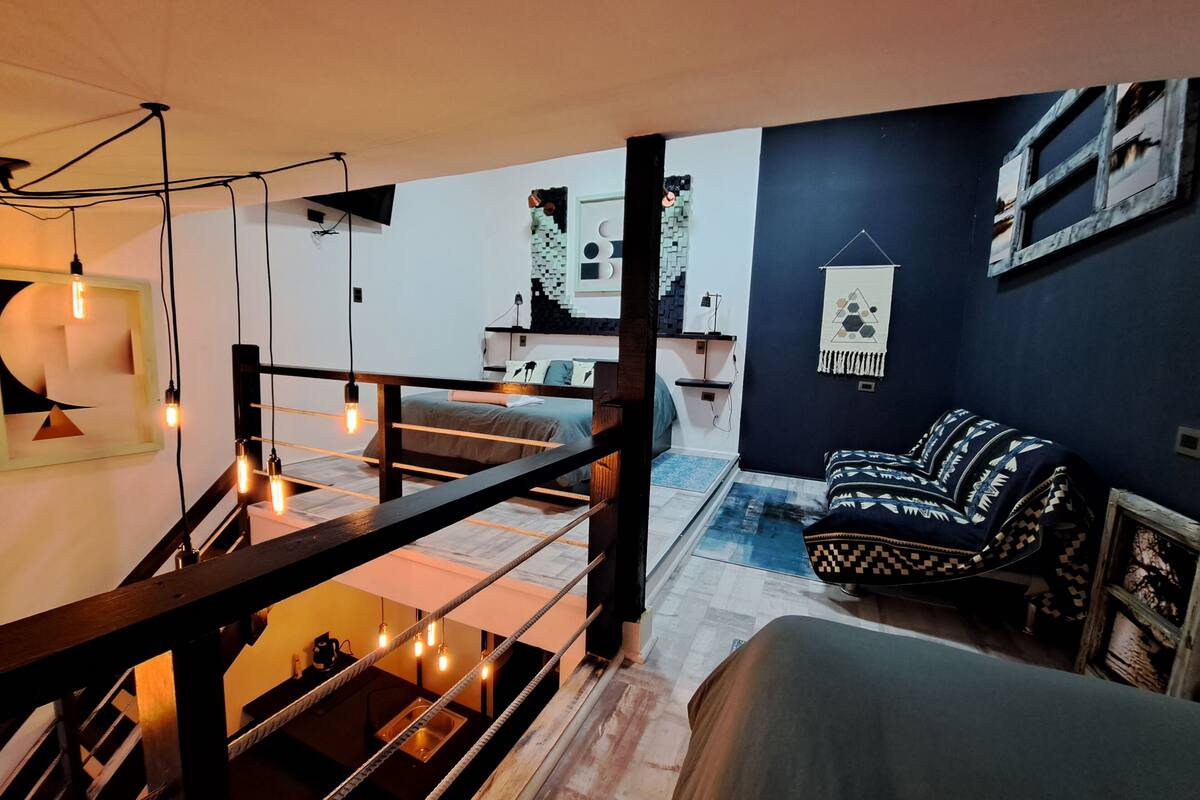 Un interior moderno con una escalera, una cama, un sofá y un televisor montado en la pared.