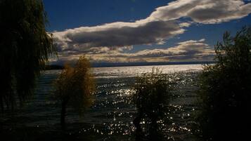 A body of water reflecting light with trees in the foreground and a cloudy sky.