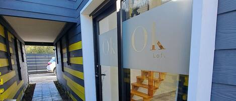 A building entrance with a checkered tile path leading to a glass door with 'Ok Loft' signage.
