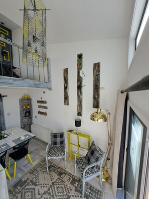 Un interior moderno con comedor, dos sillas estampadas, una mesita auxiliar amarilla, una lámpara colgante y un original aplique de techo.
