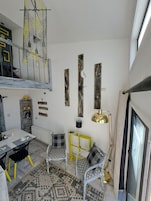 A modern interior with a dining area, two patterned chairs, a yellow side table, a hanging lamp, and a unique ceiling light fixture.