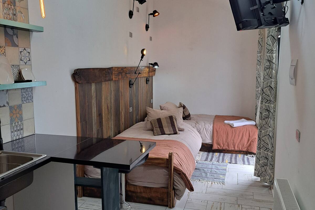 Una habitación pequeña con cama, escritorio y televisor en la pared.
