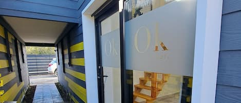 A building entrance with a checkered tile path leading to a glass door with 'Ok Loft' signage.