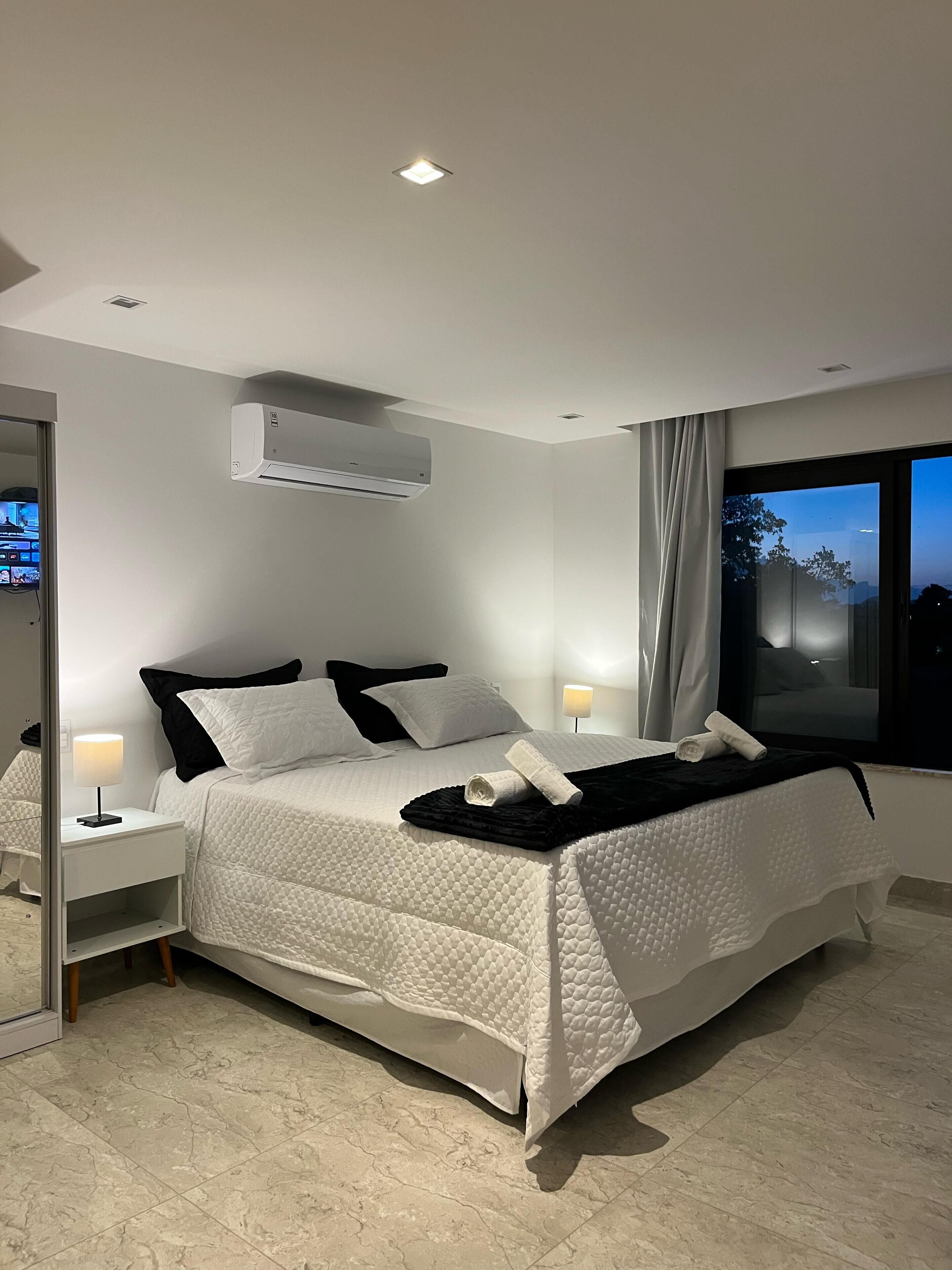 A modern bedroom with a bed, bedside tables, a mirror, and an air conditioning unit.