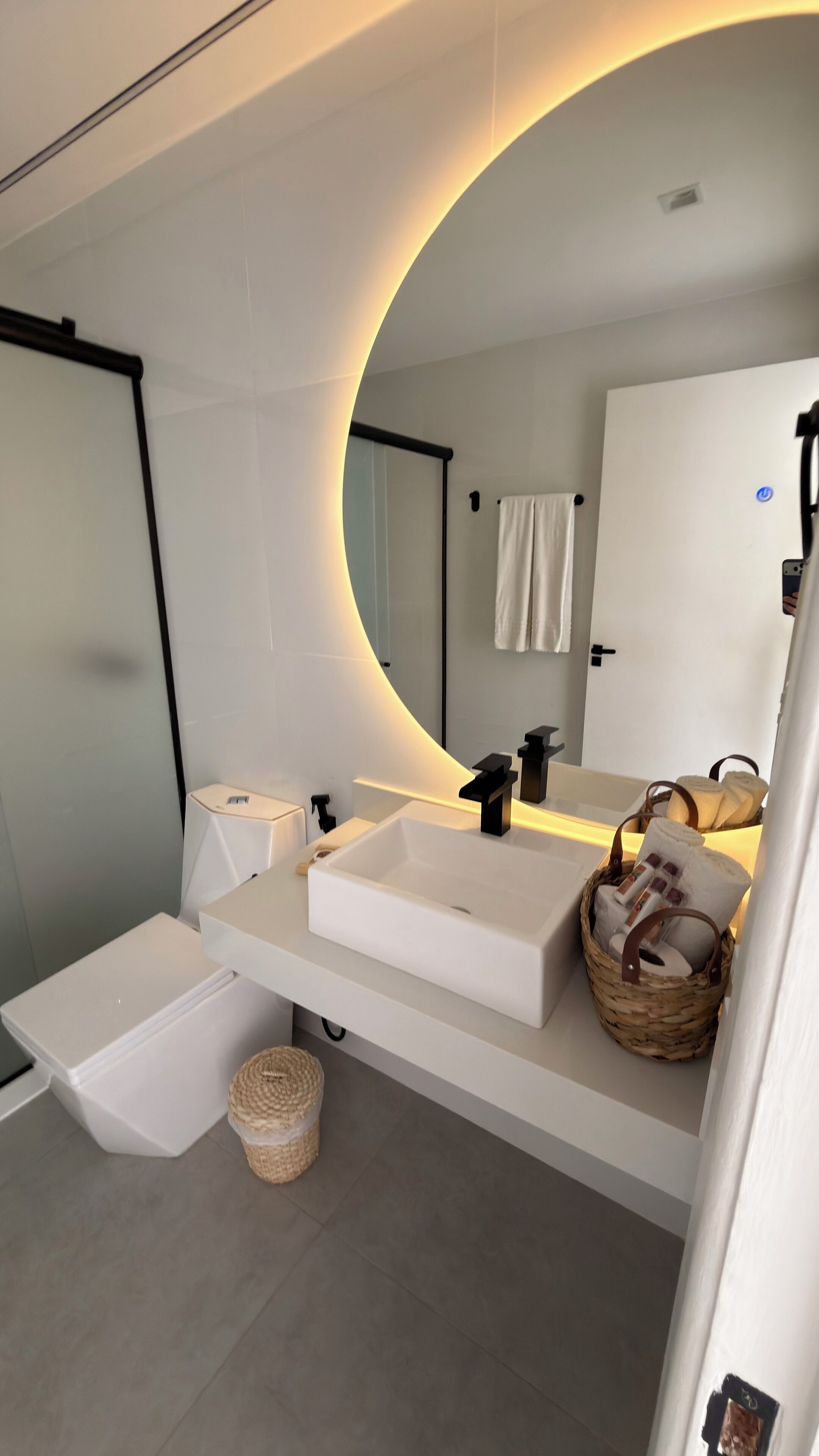 Een moderne badkamer met een gebogen spiegel, een witte wastafel en een douchehoek.