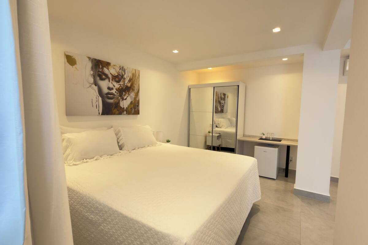 Un dormitorio moderno con una cama grande, una mesita de noche, un espejo y un pequeño escritorio con una silla.
