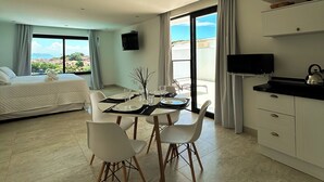 A modern hotel room with a dining area, a bed, a TV, and a balcony with a city view.