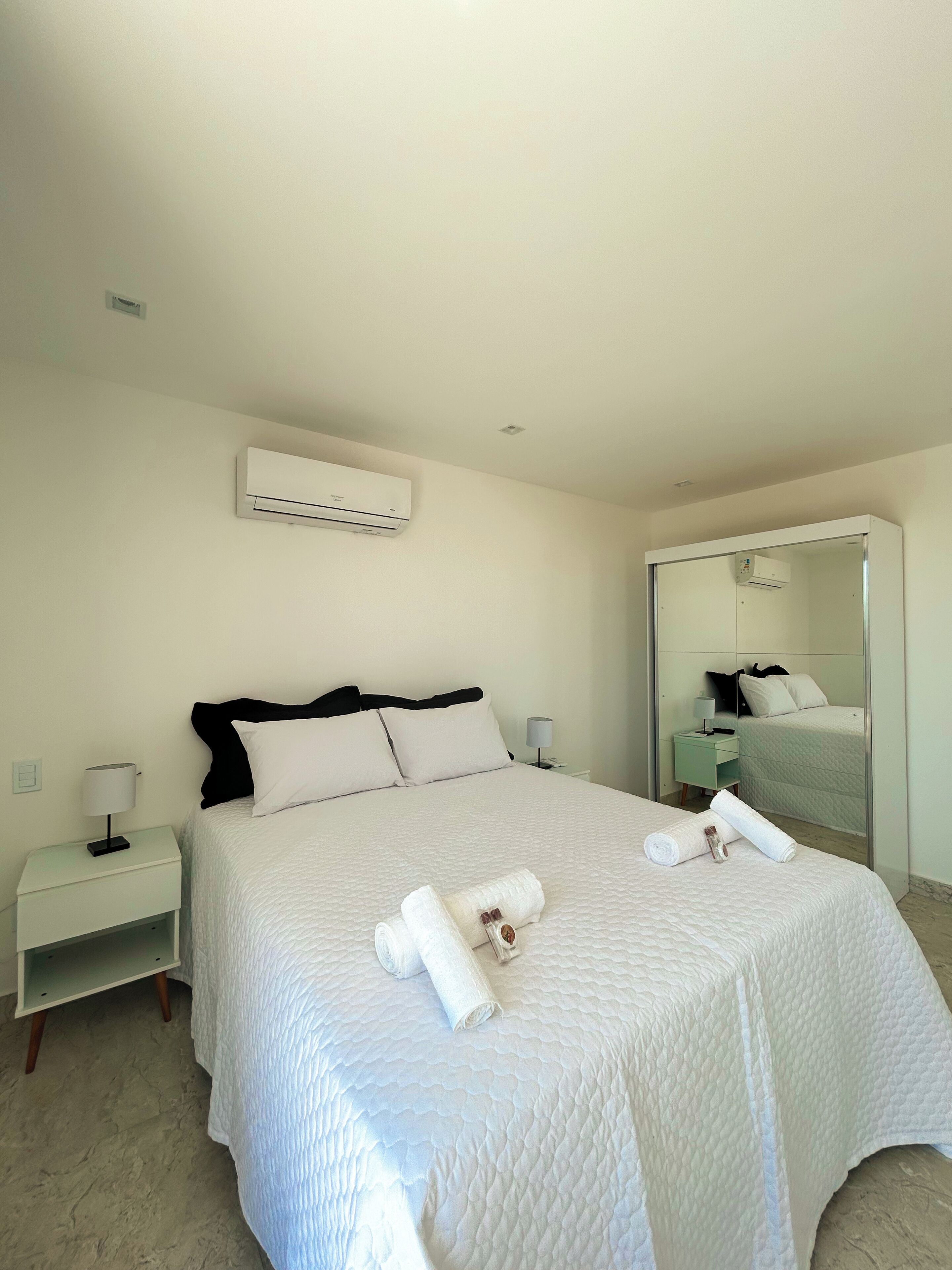 Una habitación de hotel con una cama, una mesita de noche, un aire acondicionado y un espejo.