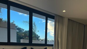 Een hotelkamer met een groot bed, meerdere kussens, een zwart-wit gestreept plaid en uitzicht op de lucht en bomen door het raam.