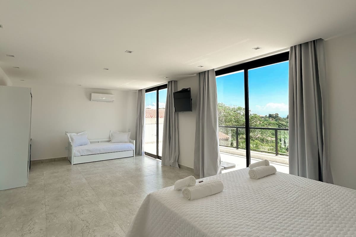 Amplia habitación de hotel con una cama grande, una zona de estar independiente con un sofá y un balcón con vistas.