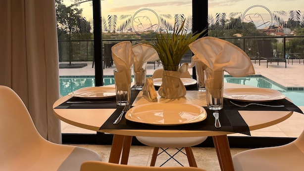A dining table set for two with a view of a swimming pool and trees.