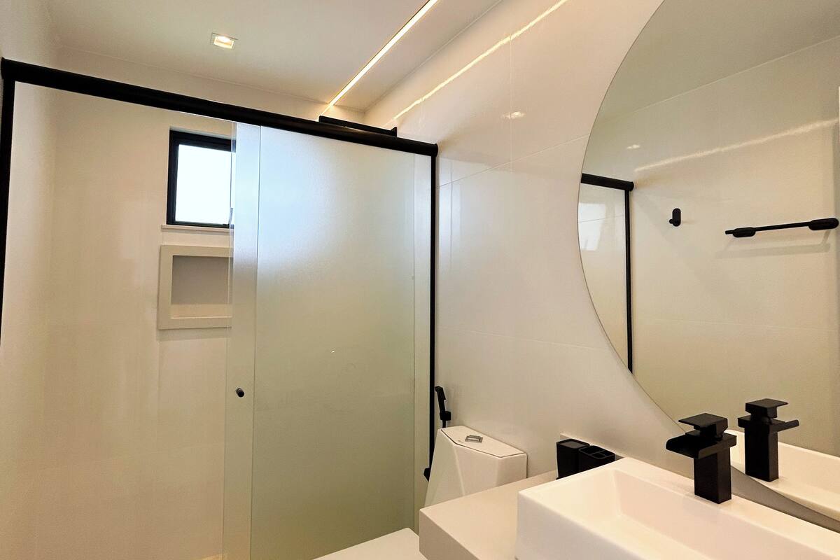Un baño moderno con un espejo grande, lavamanos blanco y cabina de ducha.