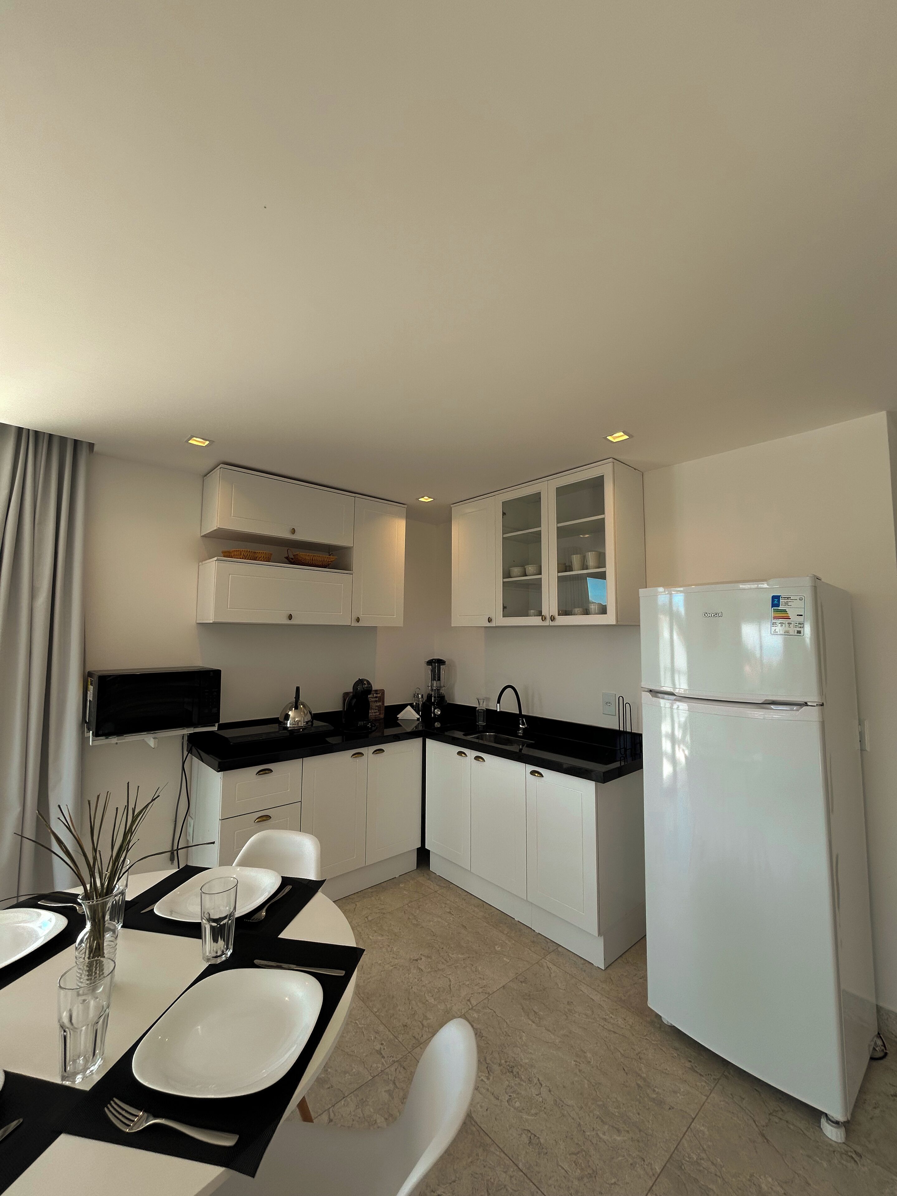 Una cocina moderna con armarios blancos, encimera negra y refrigerador blanco.