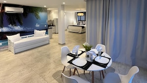 A modern living room with a white sofa, a dining table set for four, and a kitchen in the background.