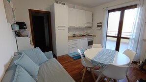A compact living space with a kitchenette, a dining area with a table and chairs, and a sofa. - Le Terrazze - Three-room apartment with terrace and shared pool on Lake Iseo (Fonteno)