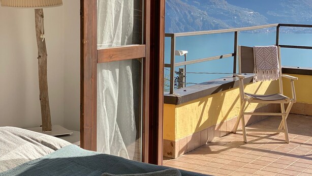 A bedroom with a bed, a chair, and a view of mountains through an open door. - Le Terrazze - Three-room apartment with terrace and shared pool on Lake Iseo (Fonteno)