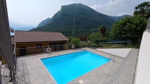 A swimming pool with a mountain backdrop, a building with a tiled roof, and a lifebuoy on the poolside. - Le Terrazze - Three-room apartment with terrace and shared pool on Lake Iseo (Fonteno)