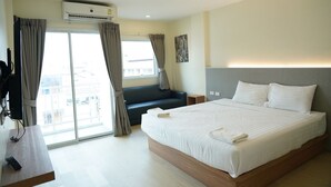 A hotel room with a large bed, a desk with a remote control, a sofa, and a sliding glass door to the outside. - Matini Premium Hotel (Thanyaburi)