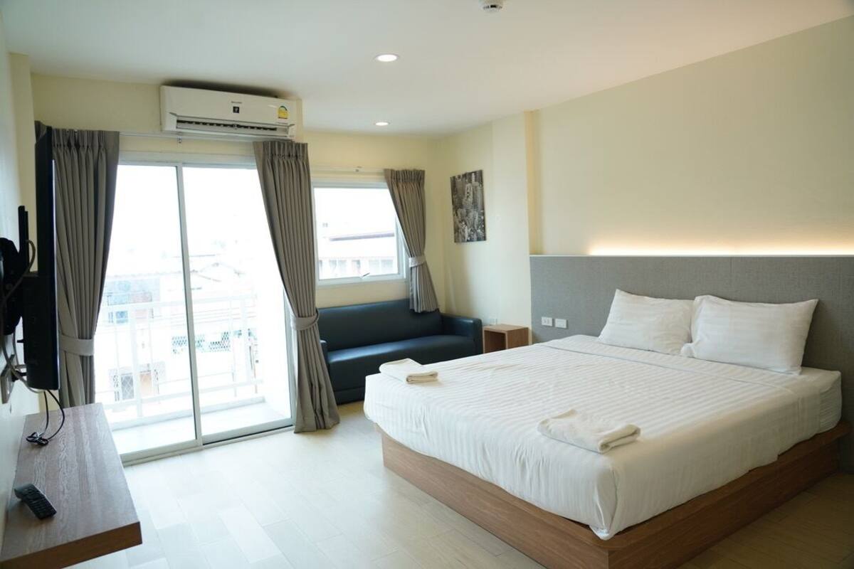 A hotel room with a large bed, a desk with a remote control, a sofa, and a sliding glass door to the outside.