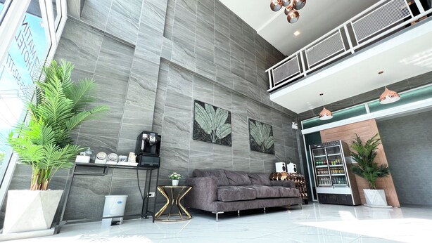A modern hotel lobby with a grey sofa, coffee machine, and decorative plants. - Matini Premium Hotel (Thanyaburi)