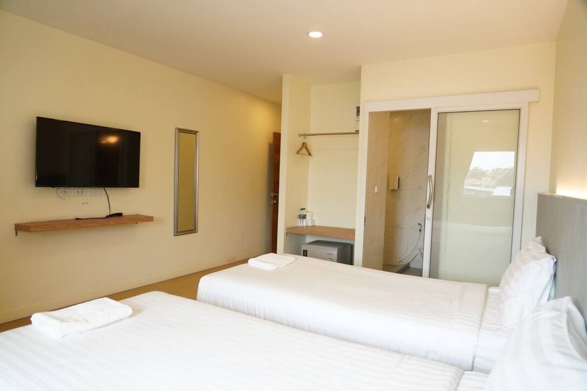 A hotel room with two beds, a TV mounted on the wall, a mirror, a bathroom with a shower, and a walk-in closet.