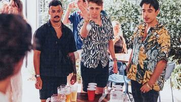 A group of people standing around a wooden table with several glasses of beer.