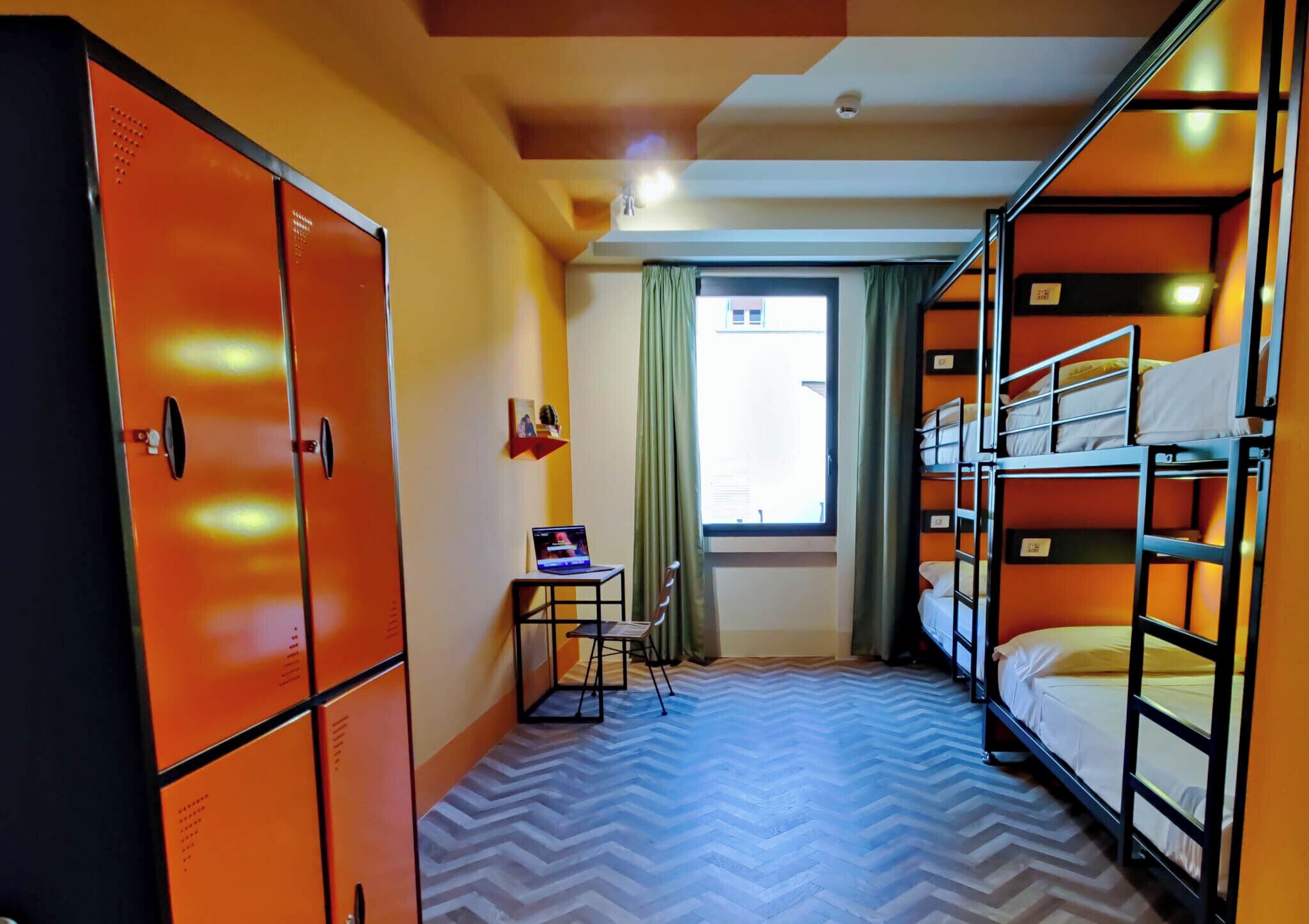 Une chambre de dortoir avec des lits superposés, un bureau avec un ordinateur portable et des casiers orange.