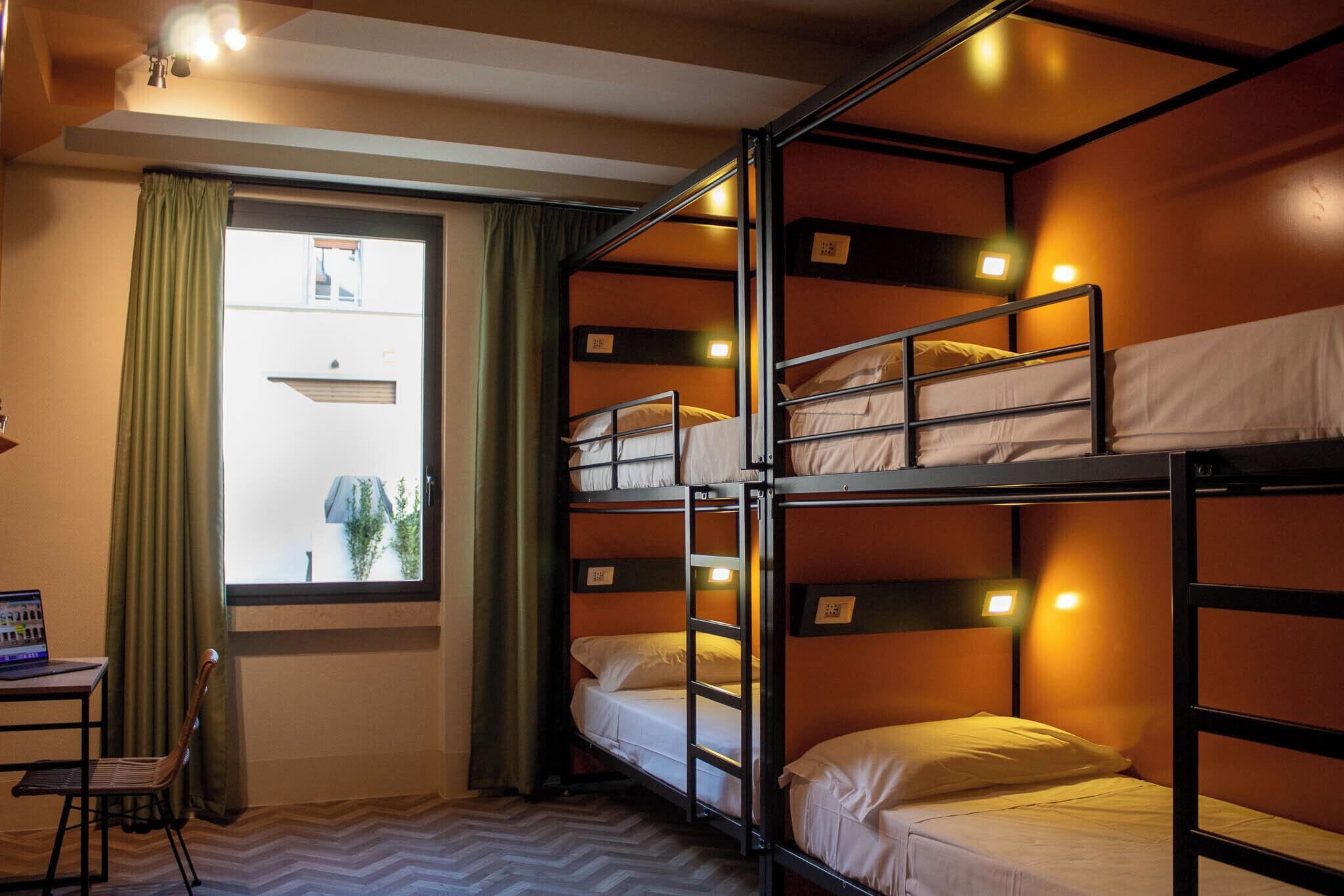 Habitación con literas, un escritorio y una silla, una ventana con cortinas y vista a un edificio.