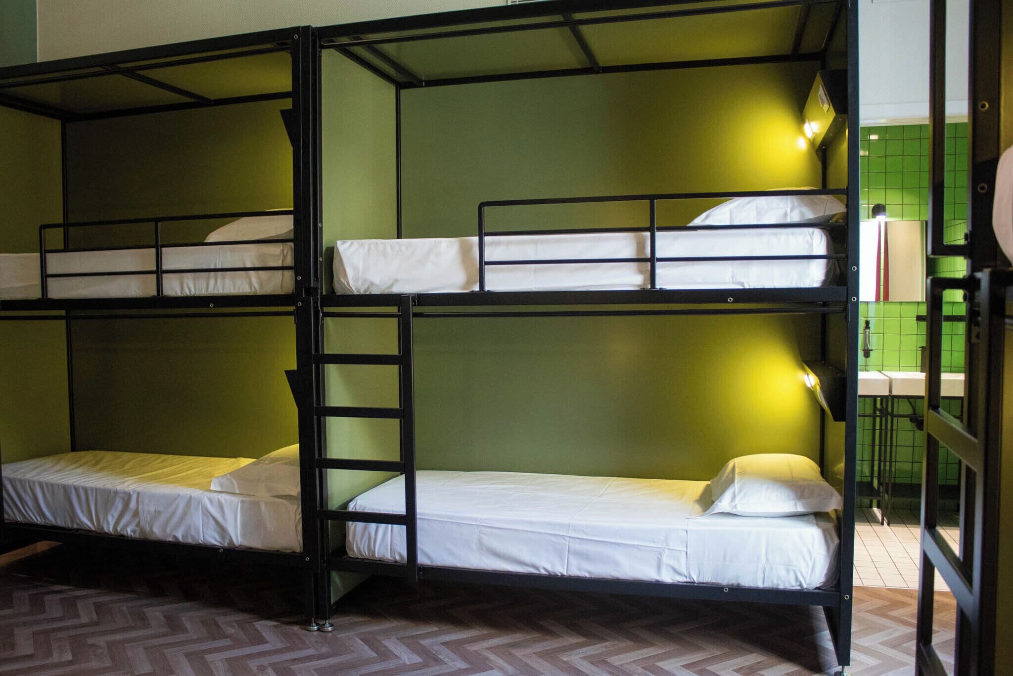 Une chambre avec des lits superposés, un plancher en bois disposé en motif chevrons, des murs verts et un miroir sur le côté droit.