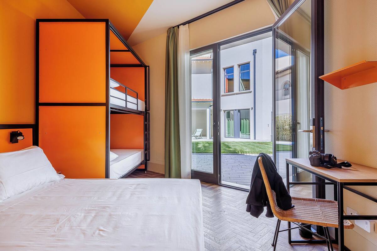 Une chambre d’hôtel avec un lit superposé, un bureau avec une chaise et une grande fenêtre donnant sur l’extérieur.